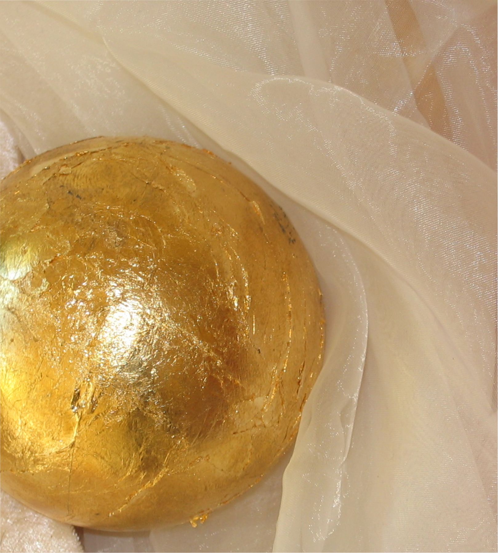 Goldene Kugel auf samtigem, beigem Tüllstoff